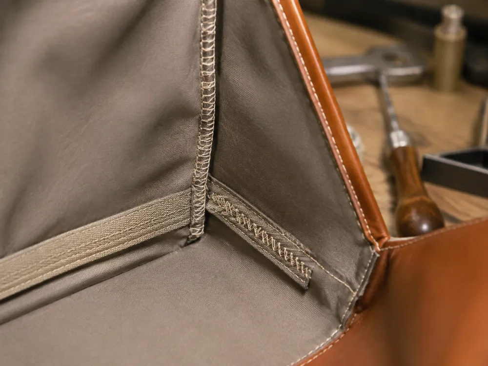 Close-up of a worker hand-stitching leather edges, showing even stitches and rich leather texture, under warm lighting